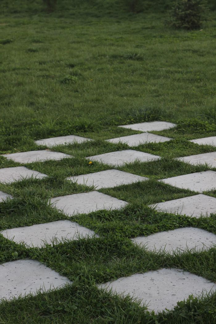 Services A pattern of concrete squares arranged on lush green grass, creating a checkered design.